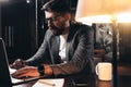 Bearded young businessman working in loft space at night. Coworker sits by the wooden table with lamp and office tools Royalty Free Stock Photo