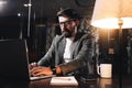 Bearded young businessman working on open space office at night. Man using modern notebook, typing text. Coworker working Royalty Free Stock Photo