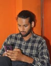 A bearded young guy with hair bun, using his phone while sitting iindoors