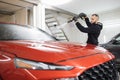 Bearded young man car wash worker spraying cleaning foam to a modern red car Royalty Free Stock Photo