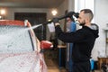 Bearded young man car wash worker spraying cleaning foam to a modern red car Royalty Free Stock Photo