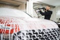 Bearded young man car wash worker spraying cleaning foam to a modern red car Royalty Free Stock Photo