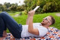 Bearded young man lying in park on blanket. He is using white ta Royalty Free Stock Photo
