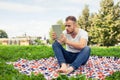 Bearded young man lying in park on blanket. He is using white ta Royalty Free Stock Photo