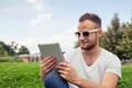 Bearded young man lying in park on blanket. He is using white ta Royalty Free Stock Photo