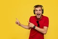 Bearded young man in red polo shirt and headphones pointing away and smiling on yellow background. Royalty Free Stock Photo