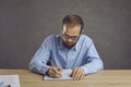 Serious young man in glasses sitting at a table and taking notes in his notebook Royalty Free Stock Photo