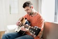 Bearded young man sitting on sofa and playing guitar Royalty Free Stock Photo