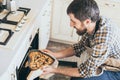 Bearded young man taking heart shaped cake out of the oven