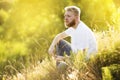 Bearded young man in white t-shirt sits on the grass on a summer day Royalty Free Stock Photo