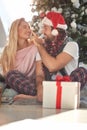 Beardy guy touching nose of his girlfriend with santa hat on his head, smiling