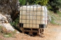 Beaten down old heavily used intermediate bulk container or IBC plastic tank with twisted metal cage put on wooden pallets Royalty Free Stock Photo