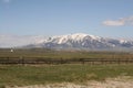 Beatiful bright day with snow covered mountains and green grassy fileds with a picket fence and farmland