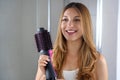 Beatiful girl holds round brush hair dryer to style hair at home. Young woman showing salon one-step hair dryer and volumizer Royalty Free Stock Photo