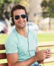 Beats on a bench - inner city living. A smiling young man wearing sunglasses sitting on a bench in a park and listening Royalty Free Stock Photo