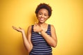 Beauitul african american woman wearing summer t-shirt over isolated yellow background Showing palm hand and doing ok gesture with Royalty Free Stock Photo