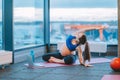 Beauteous pregnant woman in sportswear doing physical exercises, stretching on pink mat near bottle of water and laptop.