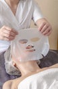 Beautician apply collagen mask to woman face. Cosmetologist works with a woman in a spa salon