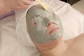 Beautician apply spoon alginate mask on the eyes and face of the girl. Purifying green mask from the dry algae. Beauty treatments