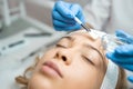 Beautician applying beauty oil mask on face skin using brush in spa salon. Woman on peeling procedure at cosmetology salon.