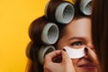 Beautician applying eye-patch to a woman with hair in rollers. close up Royalty Free Stock Photo