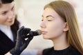 Beautician applying the tone of the foundation using special brush on face young beautiful model. Facial care and make up Royalty Free Stock Photo