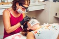 Young long-haired brunette woman putting false eyelashes on lady in beauty salon with masks