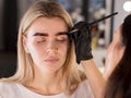 Beautician in black gloves tinting eyebrows with brush. Model with closed eyes sitting on a procedure