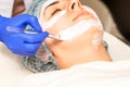 The beautician with brush applies a photochemical and glycolic peeling face mask to the female patient face in the