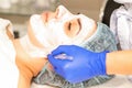 The beautician with brush applies a photochemical and glycolic peeling face mask to the female patient face in the