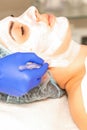 The beautician with brush applies a photochemical and glycolic peeling face mask to the female patient face in the