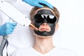 Beautician doing carbon peeling procedure to handsome guy in beauty salon. Hardware male cosmetology