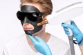 Beautician doing carbon peeling procedure to handsome guy in beauty salon. Hardware male cosmetology