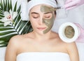 Beautician makes a face clay mask against acne on the face of a woman to rejuvenate the skin. Cosmetology treatment of problem