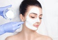 Beautician makes a face clay mask against acne on the face of a woman to rejuvenate the skin. Cosmetology treatment of problem