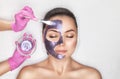 Beautician makes a face mask with purple particles on the face of a woman to rejuvenate the skin. Cosmetology treatment of problem