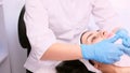 The beautician in medical gloves dabs the patient woman chin with a napkin to removes the remaining cream, cosmetology