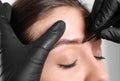 Beautician tweezing woman`s eyebrow on light background, closeup