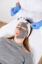 Beautician using a cosmetic brush applied a clay mask for peeling on half the face of a young woman Royalty Free Stock Photo