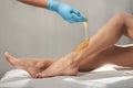 Beautician waxing female legs with liquid sugar paste in spa center.