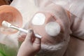 Beautician in white gloves holding a brush with cream. The girl s face is covered with a gauze bandage, and there are cotton pads Royalty Free Stock Photo