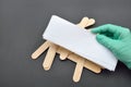 Beauticians hand with green glove holding paper tape for wax depilation, wooden spatulas for wax on black. Hair removal.