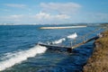 Lonely wooden pier receiving waves from the blue sea with view of the city in the background Royalty Free Stock Photo