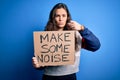 Beautiful activist woman holding banner with make some noise message over blue background pointing with finger to the camera and Royalty Free Stock Photo