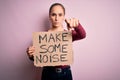 Beautiful activist woman holding banner with make some noise message over pink background pointing with finger to the camera and Royalty Free Stock Photo