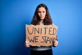 Beautiful activist woman holding banner with united stand message over blue background with a confident expression on smart face