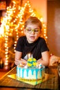 Beautiful adorable seven eight year old boy in grey shirt, celebrating his birthday, blowing candles on homemade baked cake, Royalty Free Stock Photo