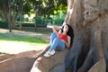 A beautiful, adult, dark-haired, curly-haired woman with the features of a Latin gypsy is lying on the roots of a giant ficus tree