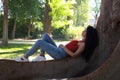 A beautiful, adult, dark-haired, curly-haired woman with the features of a Latin gypsy is lying on the roots of a giant ficus tree