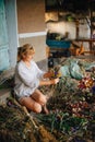 Beautiful adult female farmer sits among dried flowers and makes beautiful holiday bouquets with a serious face. Amateur florist c